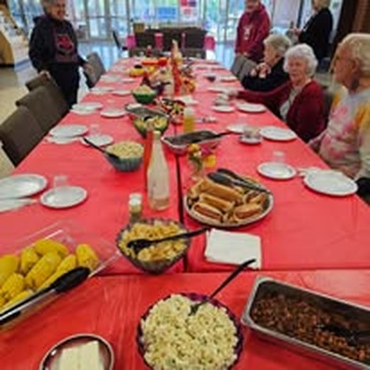 A long table covered in a red cloth, laden with food as community members gather to eat